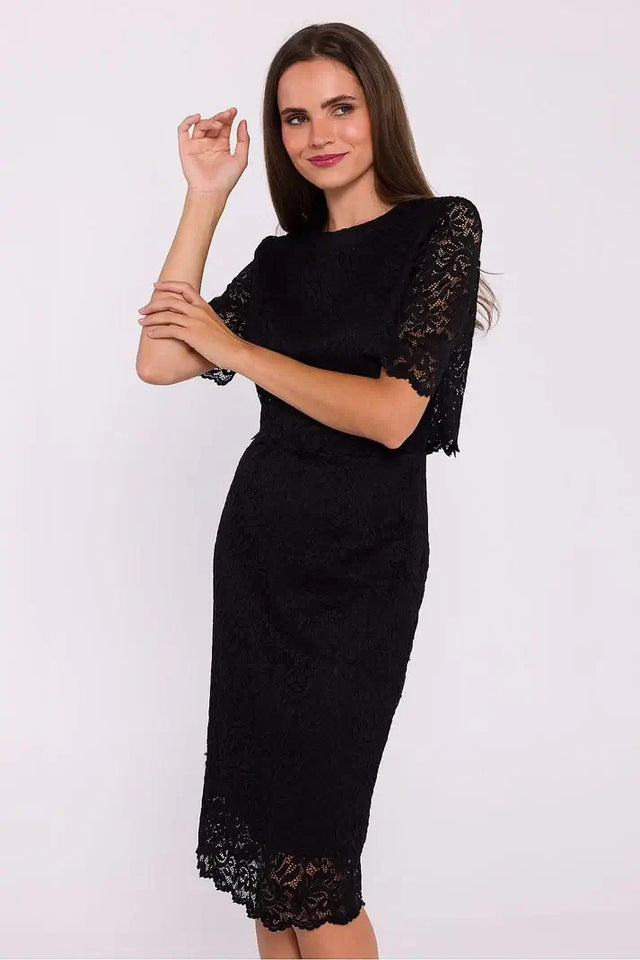 Elegant woman wearing a black lace midi dress with short lace sleeves and a delicate floral pattern, posing stylishly against a plain white background.