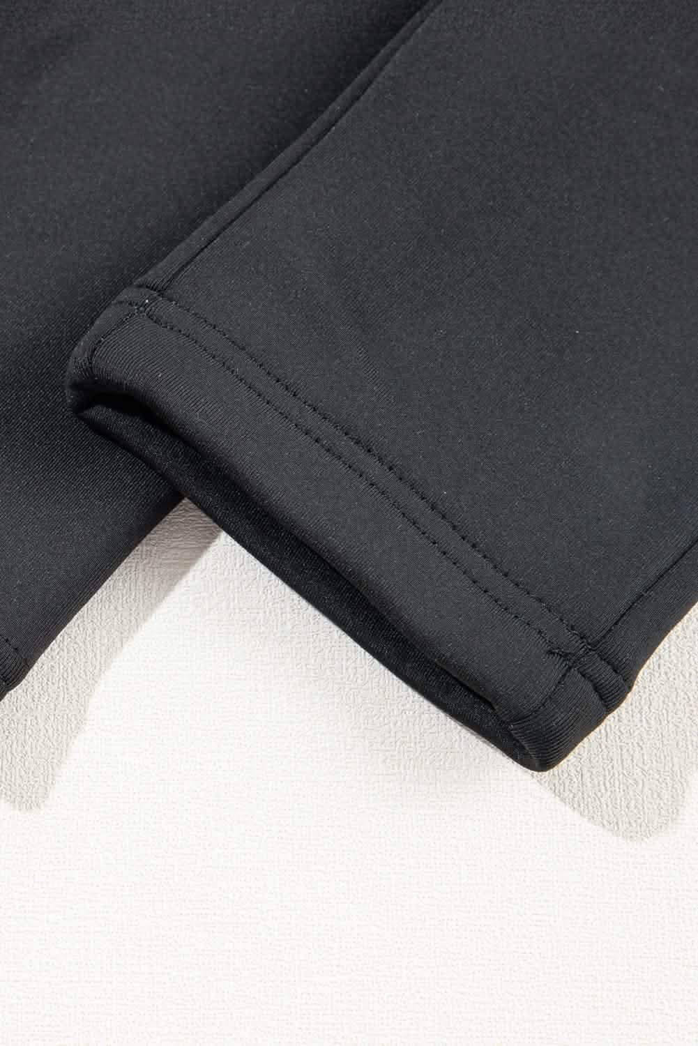 Close-up of the hem detail of black high-waist sport leggings, showcasing smooth stitching and soft fabric texture.