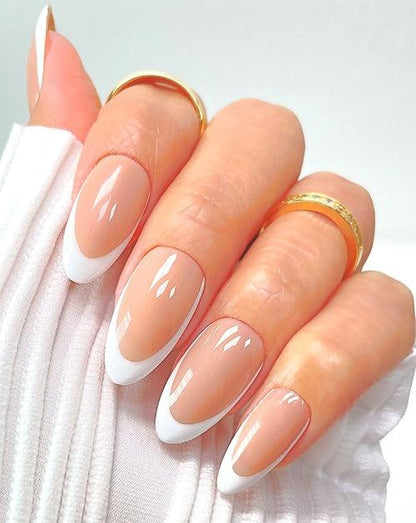 A hand with long, almond-shaped nails featuring a French manicure. The tips are white, and the base is a natural pink. The person is wearing gold rings and a white, pleated cuff on their wrist.