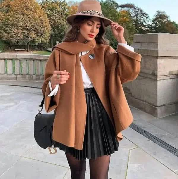 Stylish camel-colored wool coat paired with a pleated black skirt and brown fedora hat.