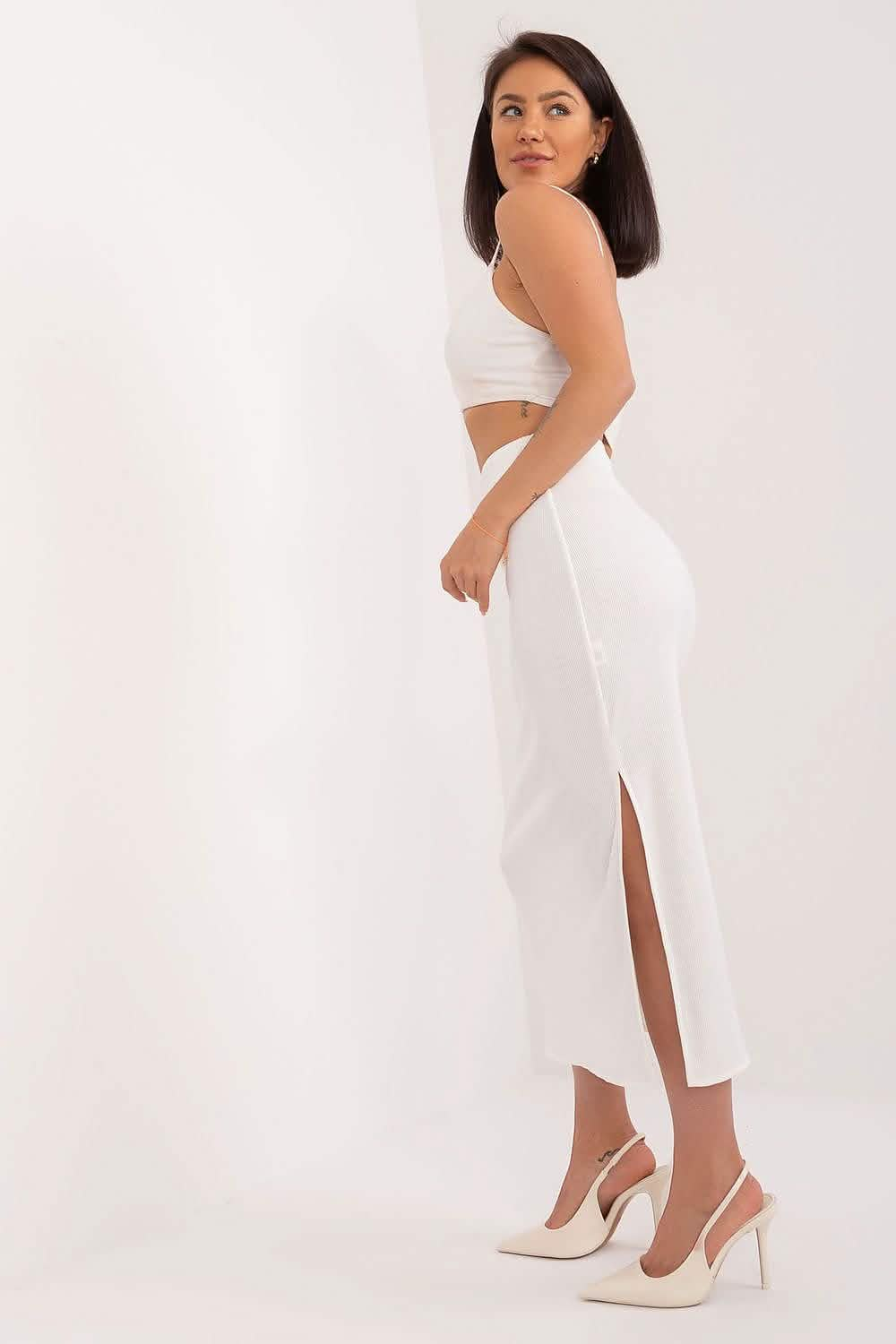 White two-piece outfit consisting of a crop top and side-slit midi skirt paired with cream heels.