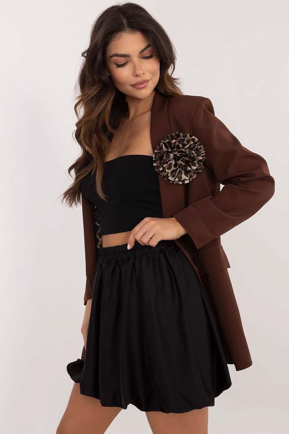 A brown blazer with a decorative brooch worn over a black strapless dress.