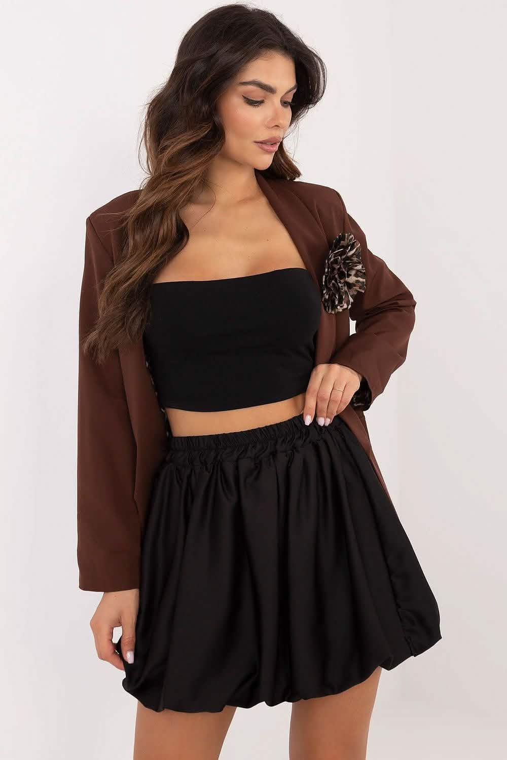 A brown jacket worn over a black crop top and bubble skirt outfit.