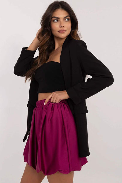 A woman wearing a black blazer, black crop top, and magenta pleated skirt.