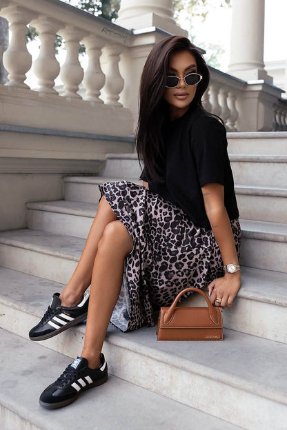 Fashionable outfit combining a black top, leopard print skirt, sneakers and brown handbag.