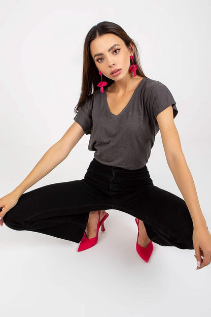 A person wearing a gray t-shirt, black pants and red heels in a seated pose.