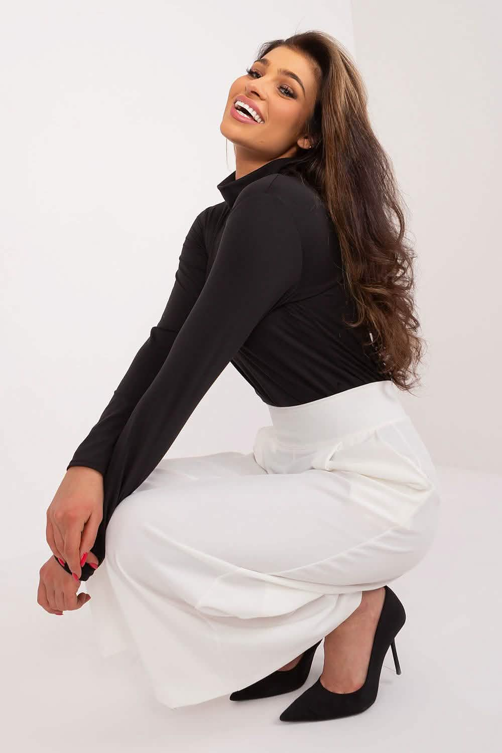 A woman in a black turtleneck and white skirt crouching in high heels.