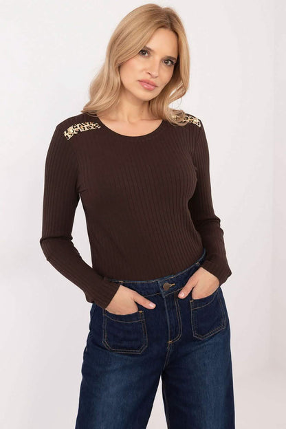 A brown ribbed sweater with decorative shoulder details paired with dark blue jeans.