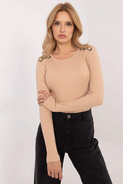 Beige long-sleeved top with decorative shoulder details paired with black pants.