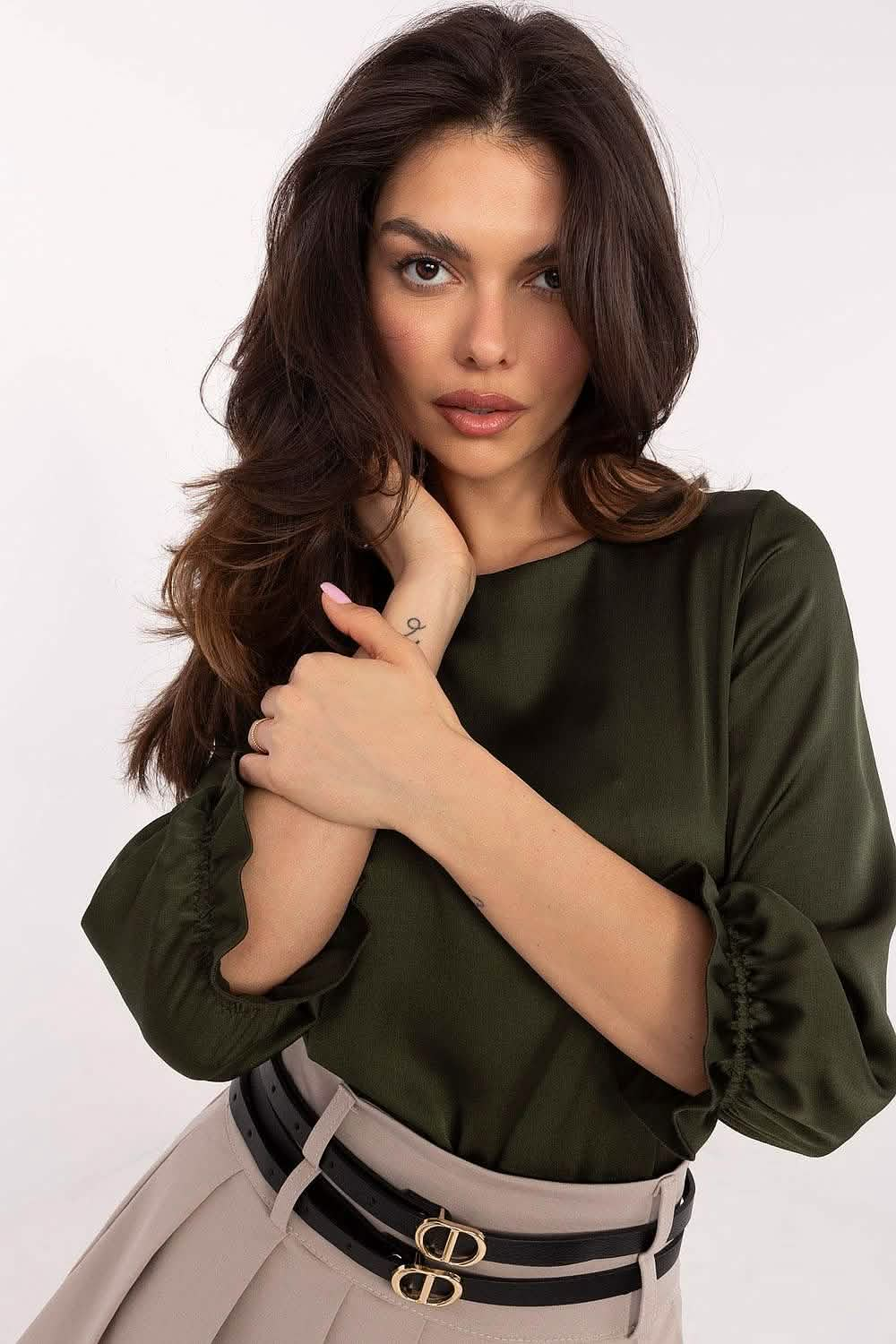 A woman wearing a dark green sweater and belted high-waisted pants.