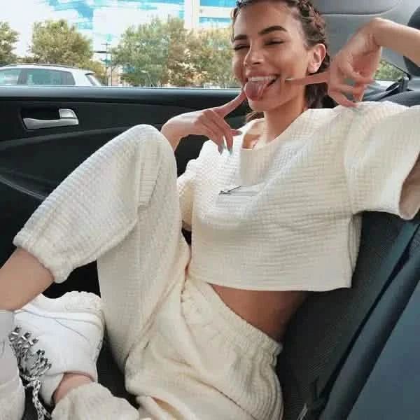 A person wearing a white crop top and matching sweatpants relaxing in a car’s backseat.