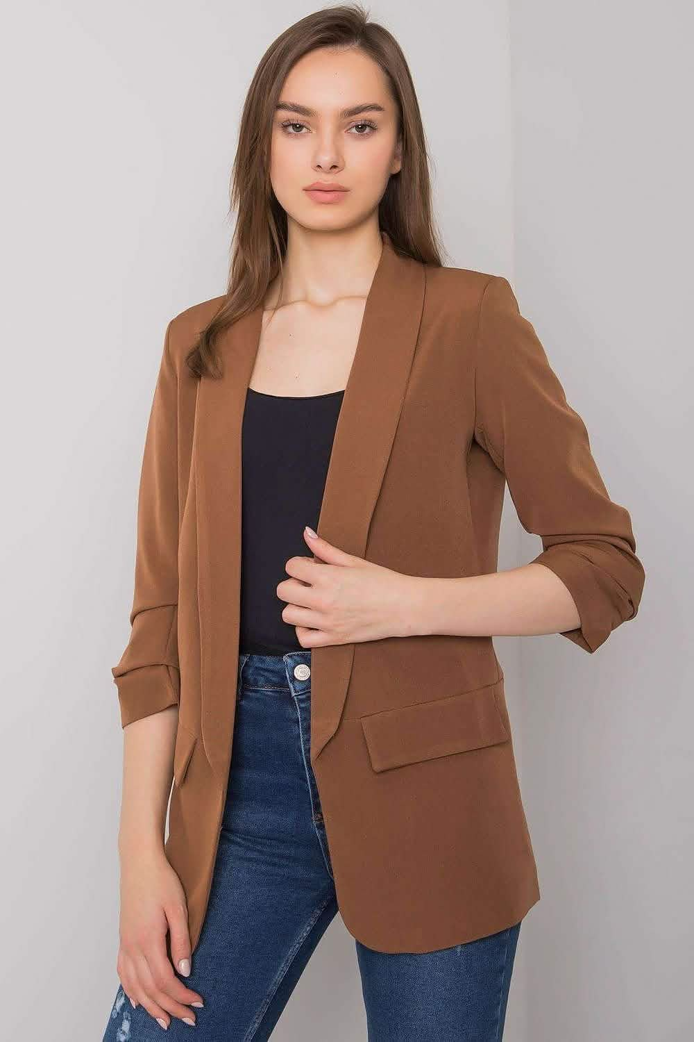 A brown blazer with rolled sleeves worn over a black top and blue jeans.