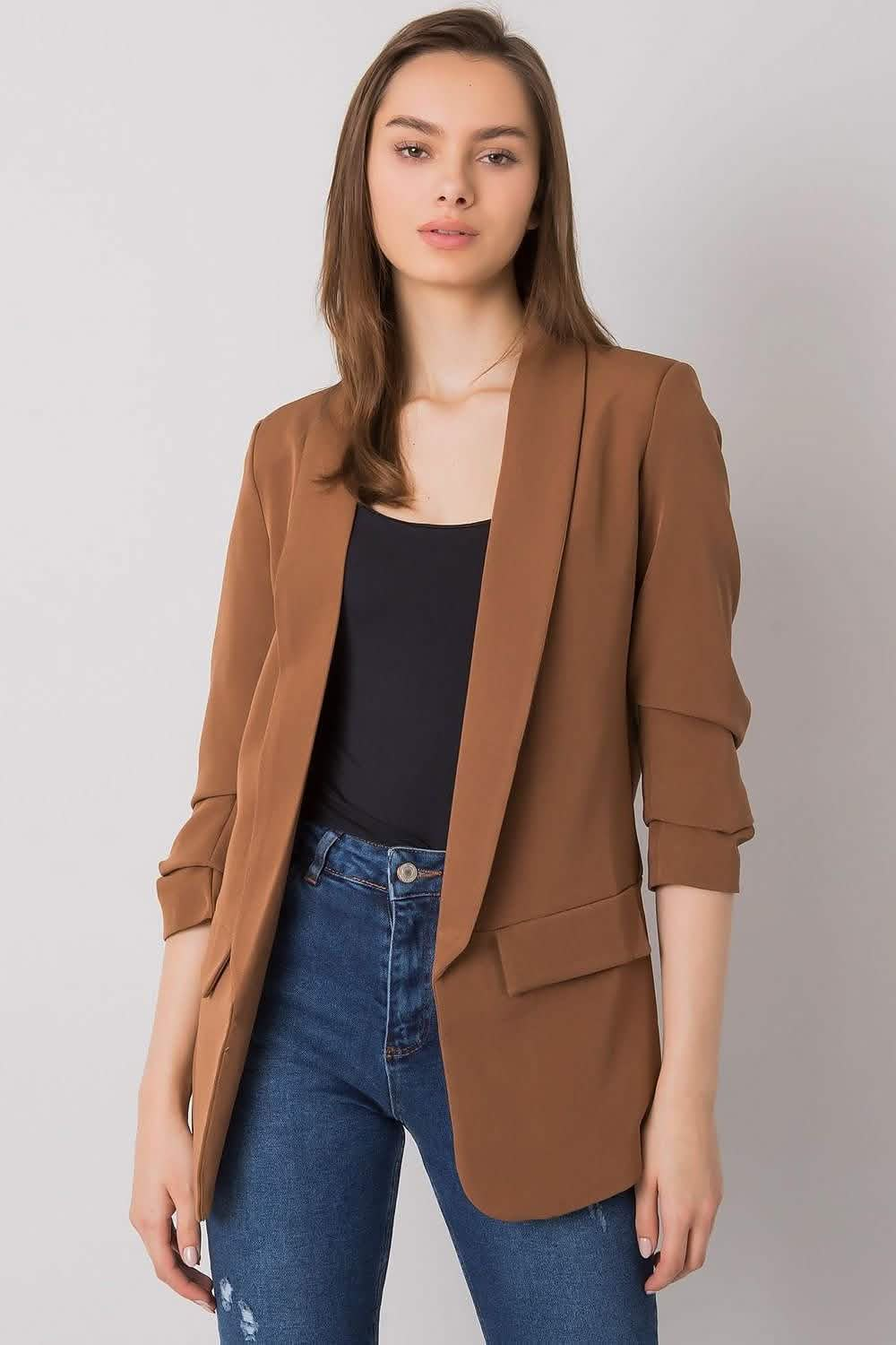 Camel-colored blazer with ruched sleeves worn over a black top and blue jeans.