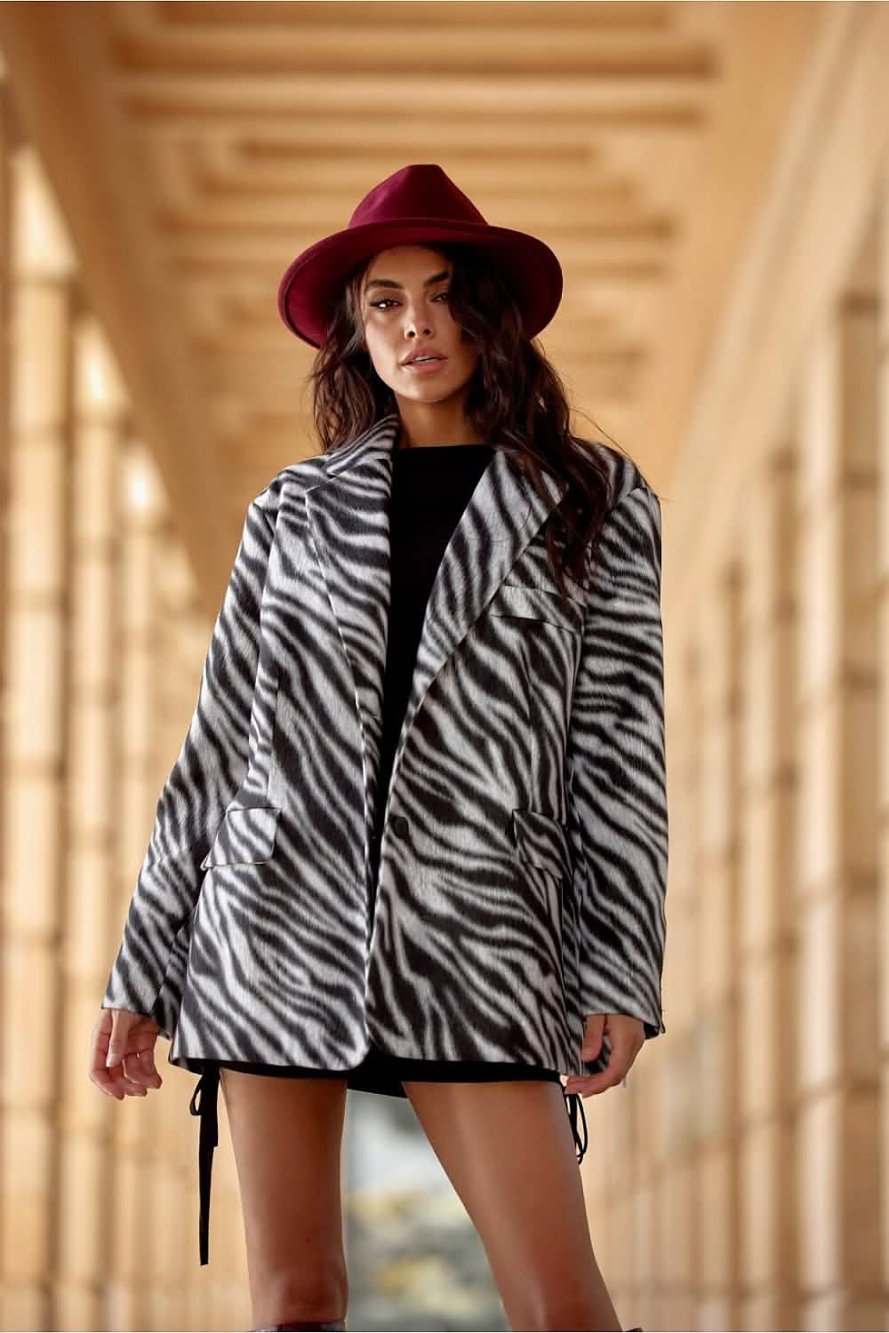 Zebra-print coat with black trim worn with a burgundy fedora hat.